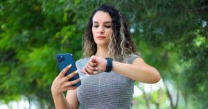 A woman looks at her smartwatch while holding a mobile