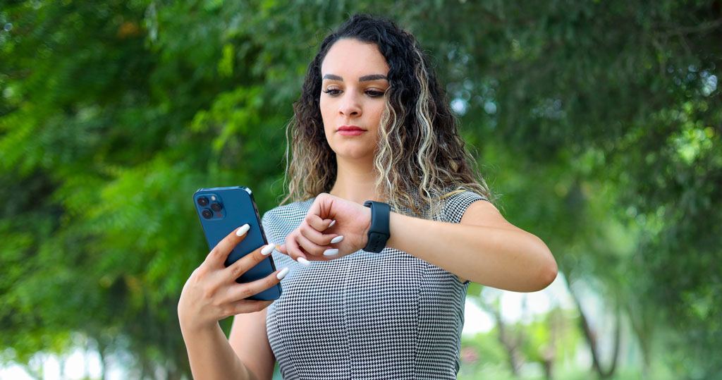 A woman looks at her smartwatch while holding a mobile
