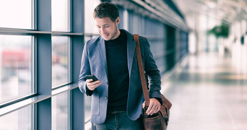 A man looks at a smartphone and walks through an airport
