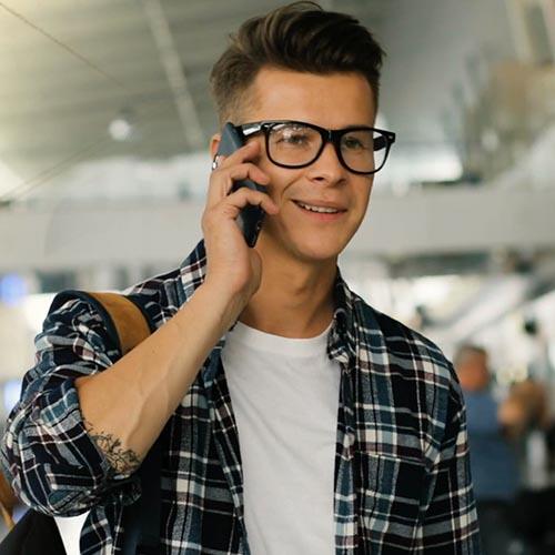 Young man wearing flannel shirt and glasses talking on mobile in airport using eSIM roaming | Workz Group